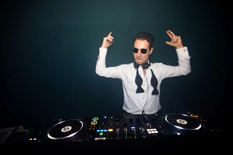 DJ met beide armen omhoog achter de draaitafels
